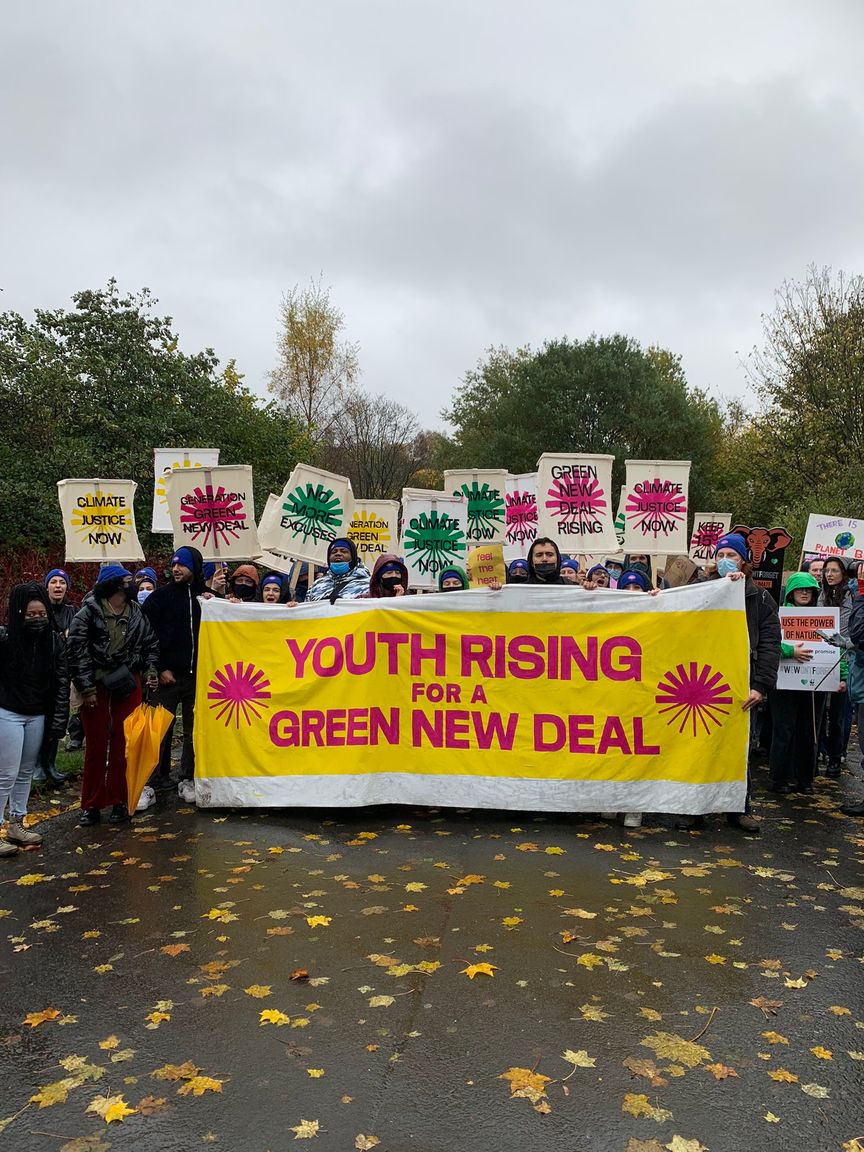 A group of young people hold up Green New Deal Rising signs and a large banner