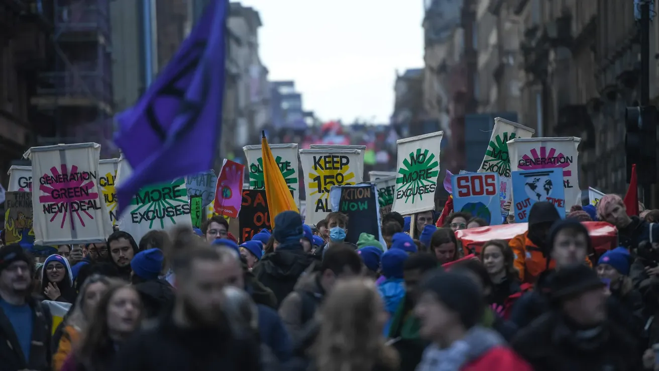 A group of people walk through a city street, holding up Green New Deal Rising signs